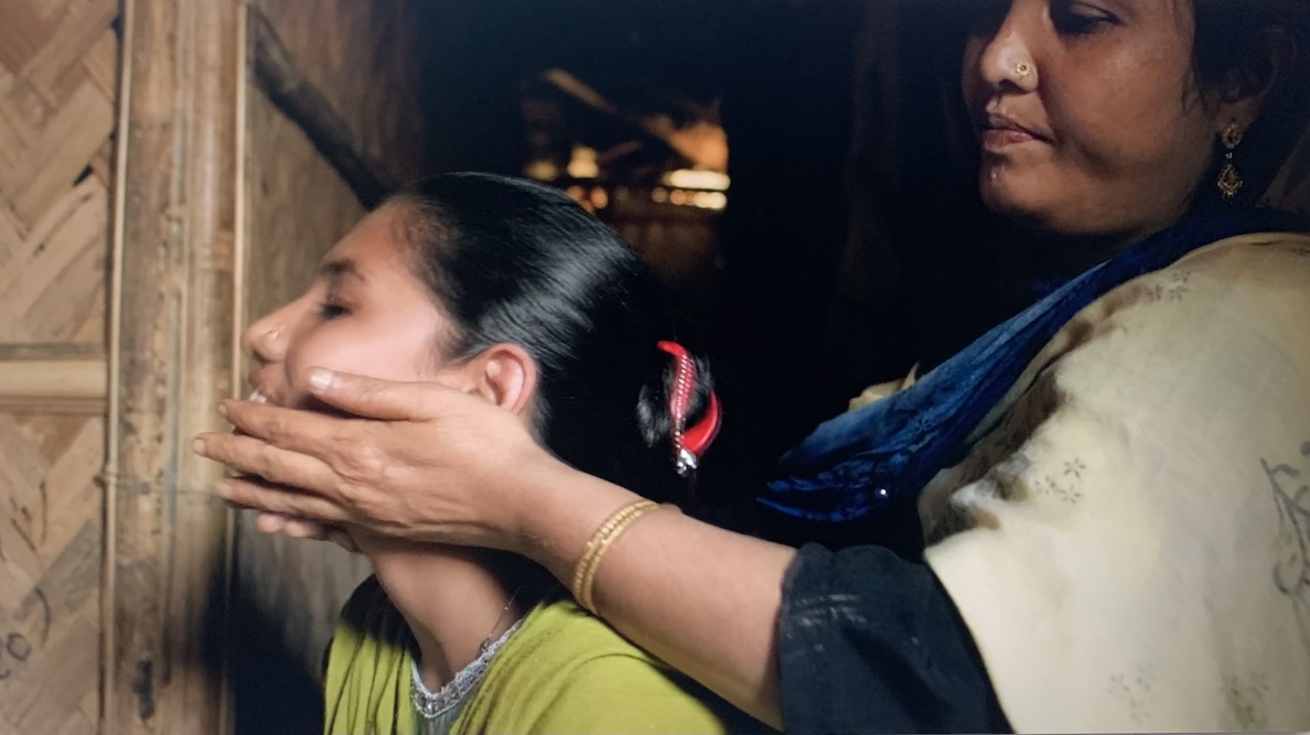 Screenshot from the film, Wandering: A Rohingya Story, showing a Rohingya mother smoothing her hands over her daugher's laughing face.